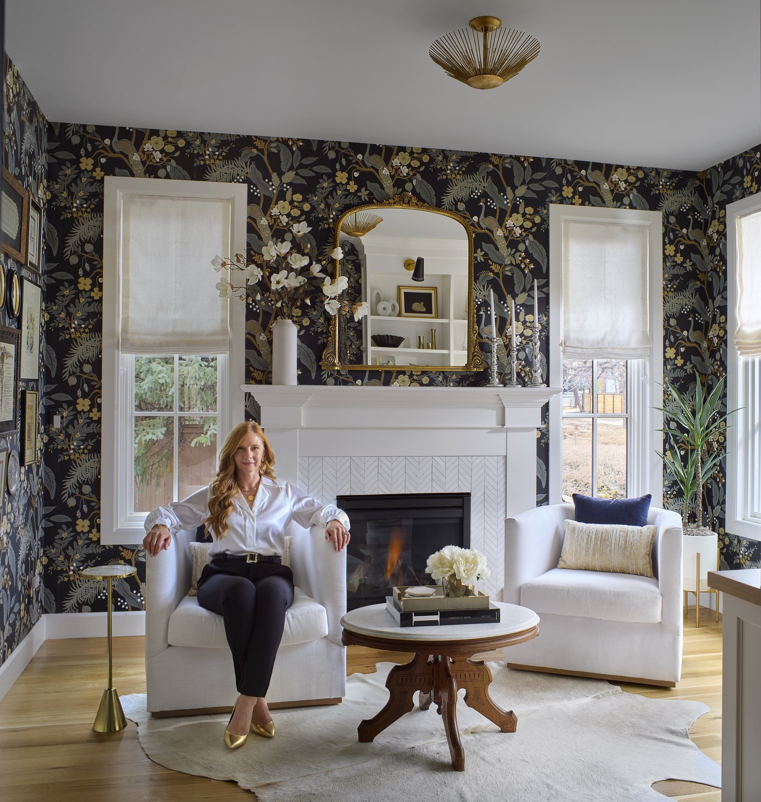 Kendra Stewart, Founder and Principal Interior Designer of E+E Design Consulting, seated by a fireplace.