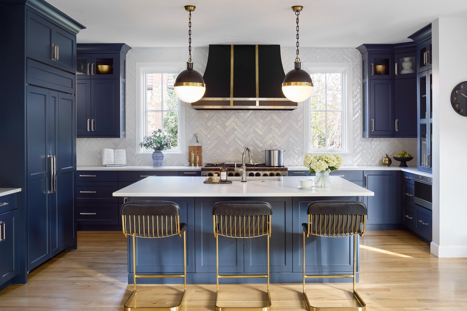 Navy cabinetry, brass-trimmed black range hood and lit globe pendants in the Bonnie Brae whole-home remodel kitchen in Denver.