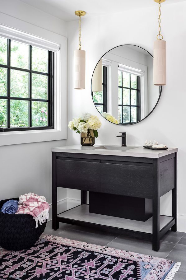 Black vanity with a round mirror, blush pendant and patterned rug in a bathroom of the Greenwood Village whole-home remodel.