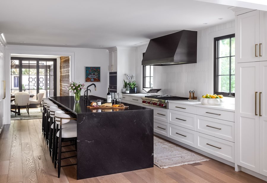 Black stone waterfall island with white perimeter cabinetry and a black range hood in the Greenwood Village whole-home remodel kitchen.
