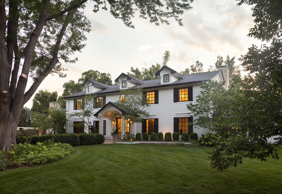 White two-story home with black-shuttered windows glowing at dusk in the Greenwood Village whole-home remodel, Colorado.