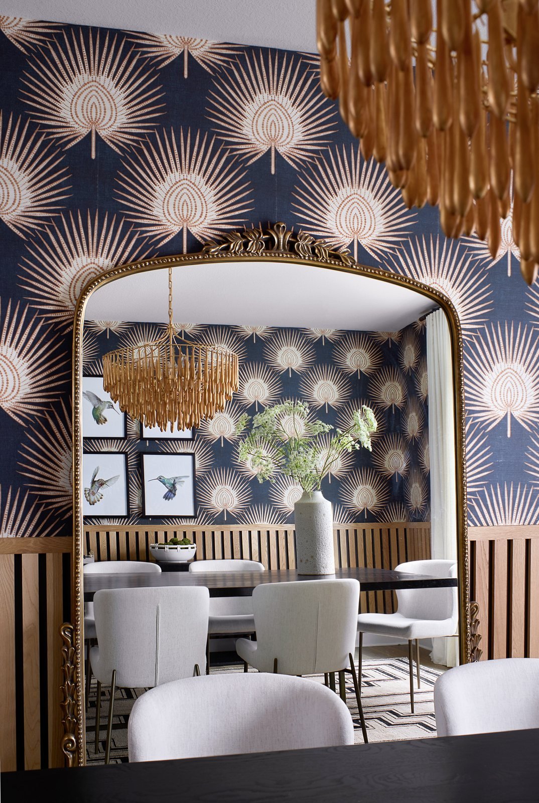 Ornate brass mirror reflecting the dining table and beaded chandelier against fan-motif wallpaper in The Canyons dining room, Castle Pines.