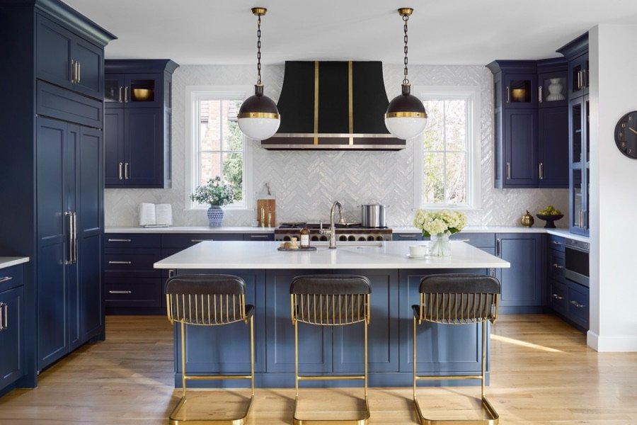 Navy island kitchen with brass hardware, black-and-gold hood, and white herringbone backsplash designed by E+E in Denver