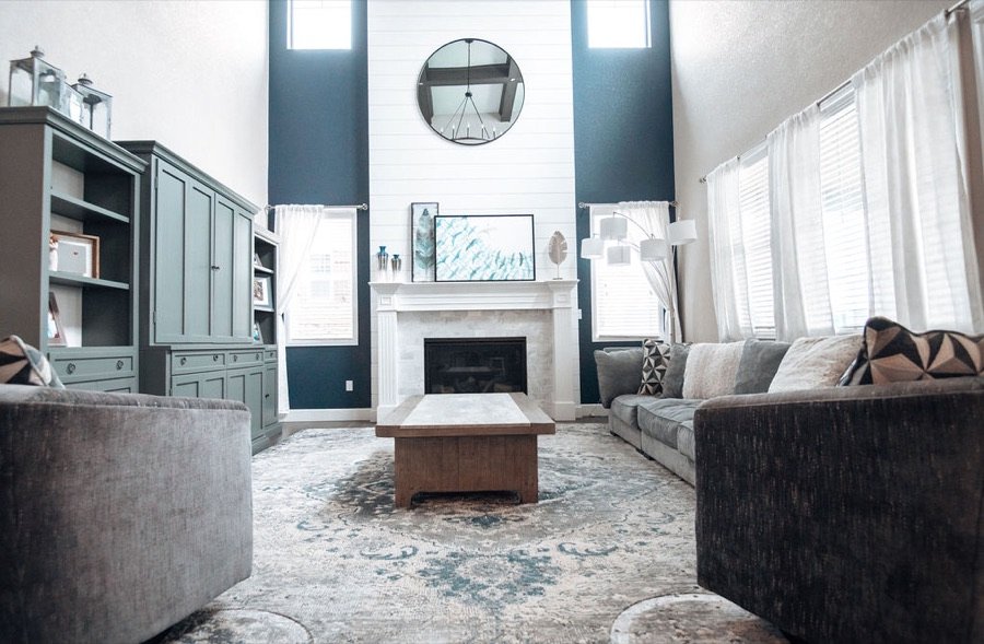 Double-height family room with faux wood beams, shiplap fireplace wall, and gray sectional, Blackstone family room renovation in Aurora, Colorado