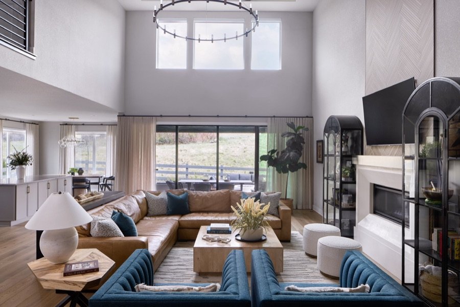 Great room of The Canyons new build in Castle Pines with tan leather sectional, blue chairs, arched display cabinets, and open kitchen